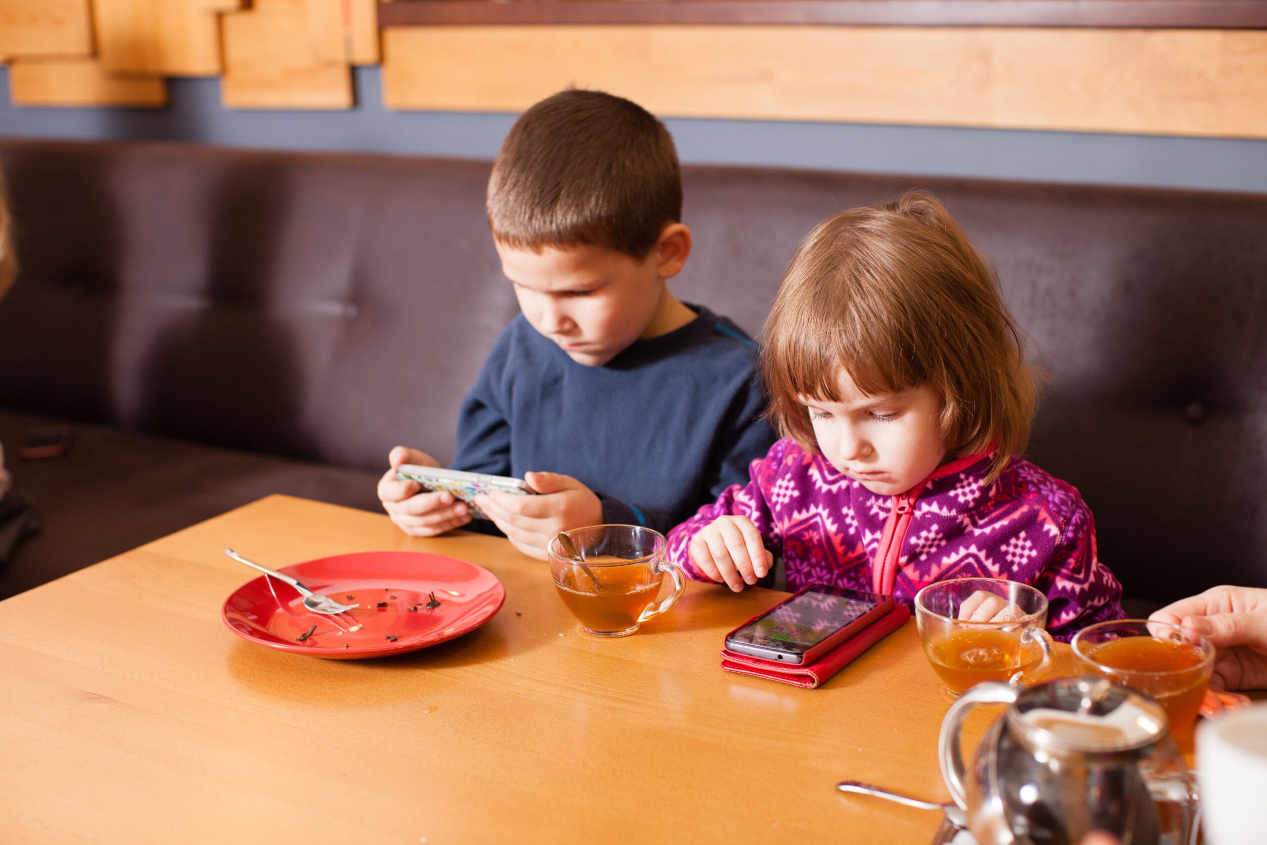 Children are playing games on smartphones while parents having a conversation.